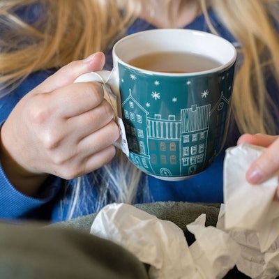 Eine Frau trinkt Tee und hält ein Taschentuch in ihrer Hand. (Symbolfoto)