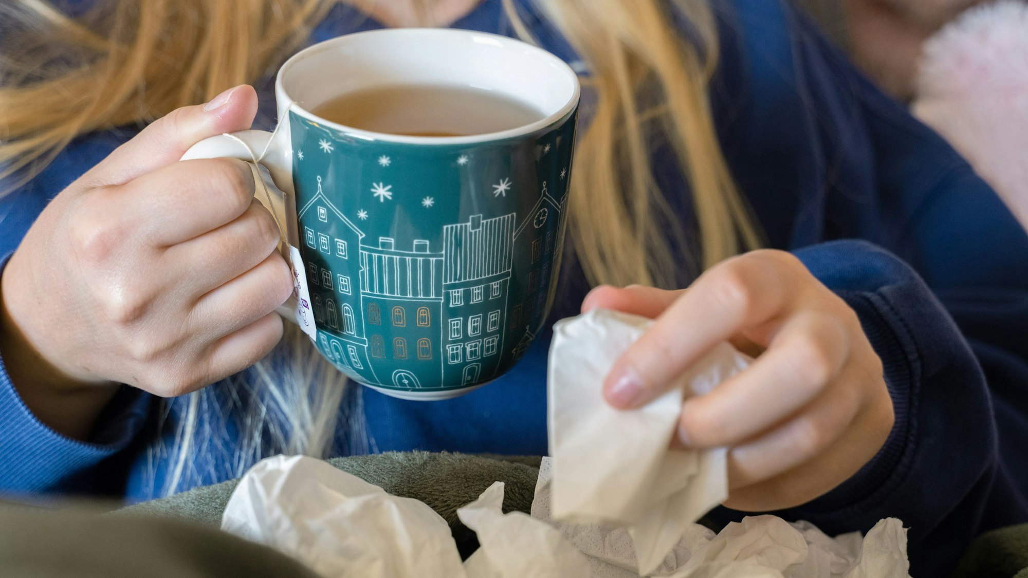 Eine Frau trinkt Tee und hält ein Taschentuch in ihrer Hand. (Symbolfoto)