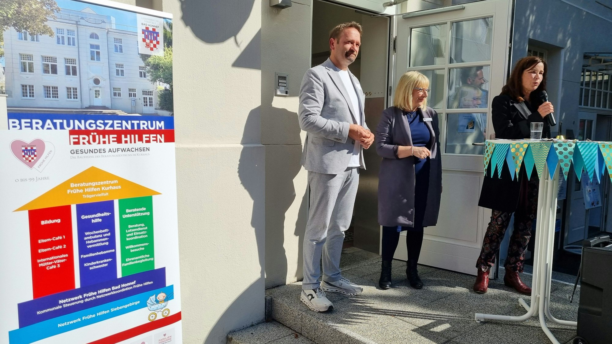 Ein Mann und zwei Frauen an einem Stehtisch, am Rand ein Plakat mit Informationen über das Beratungszentrum.
