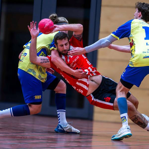 Von hinten umklammert ein Gegenspieler aus Eschweiler den werfenden David Henzel, dessen Bauch zu sehen ist.