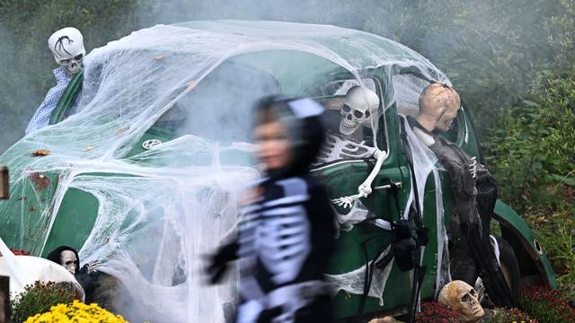 Ein Kind geht an einem zu Halloween mit Netz und Skeletten geschmückten alten VW Käfer vorbei. (Archivbild)