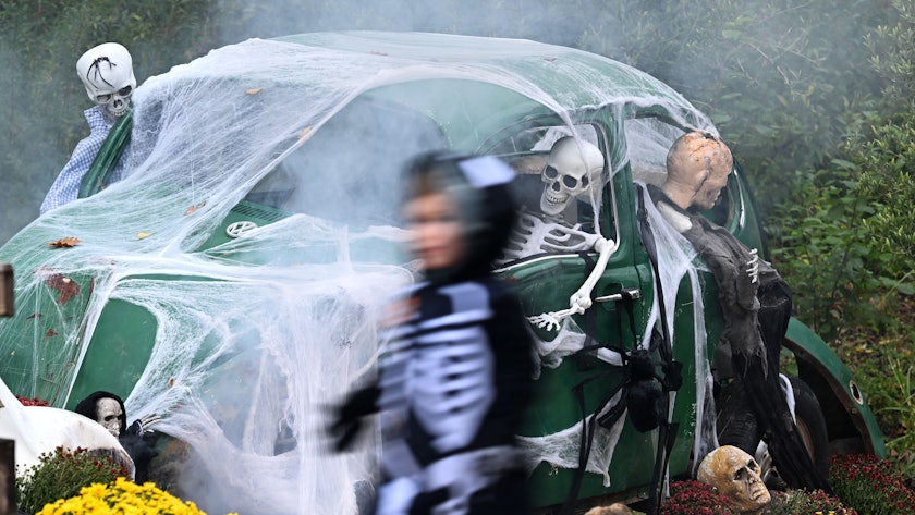 Ein Kind geht an einem zu Halloween mit Netz und Skeletten geschmückten alten VW Käfer vorbei.