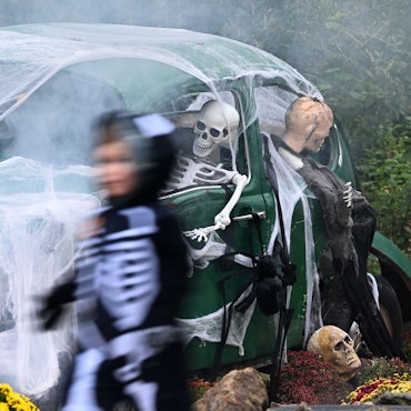 Ein Kind geht an einem zu Halloween mit Netz und Skeletten geschmückten alten VW Käfer vorbei.