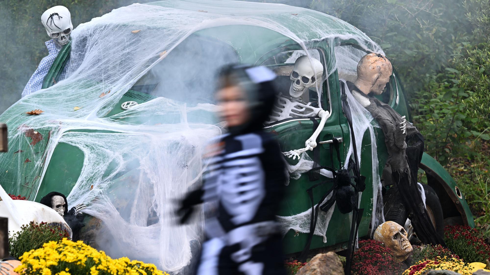 Ein Kind geht an einem zu Halloween mit Netz und Skeletten geschmückten alten VW Käfer vorbei.