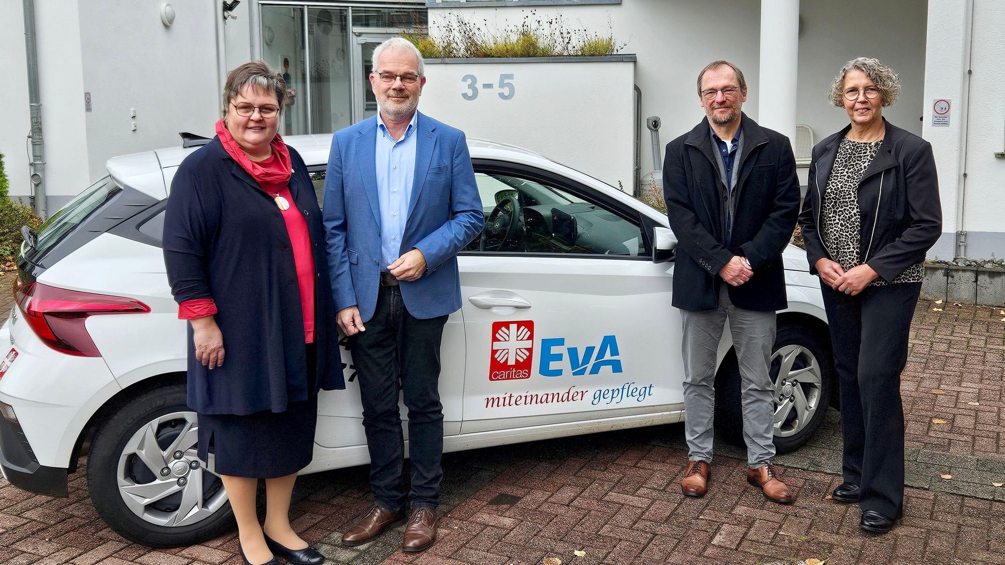 Ute Stolz, Malte Duisberg, Pfarrer Christoph Ude und Elisabeth Nosbers stehen vor einem neuen Wagen, den beide Logos zieren.