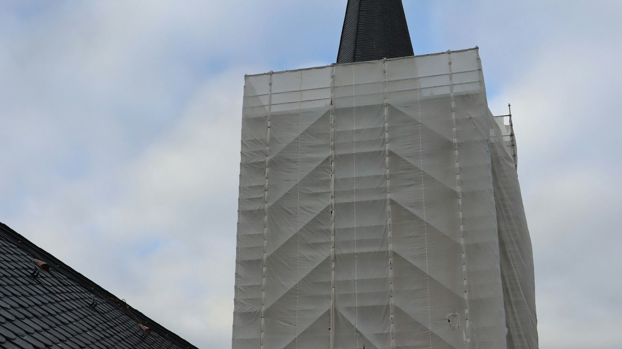 Zu sehen ist ein Kirchturm, der in ein Schutznetz gehüllt ist.