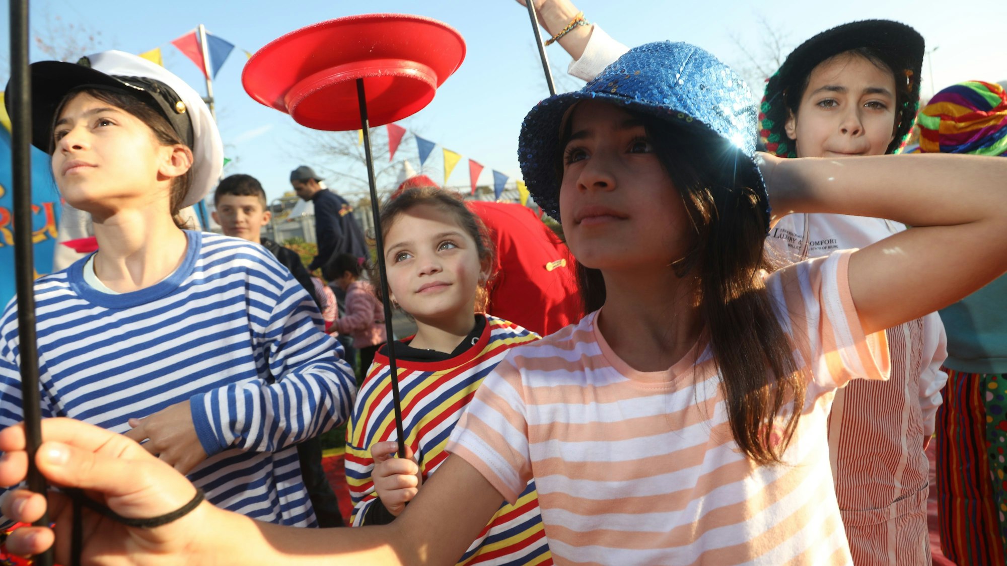 Kinder mit geringelten T-Shits und Hüten jonglieren Teller auf einem Stab