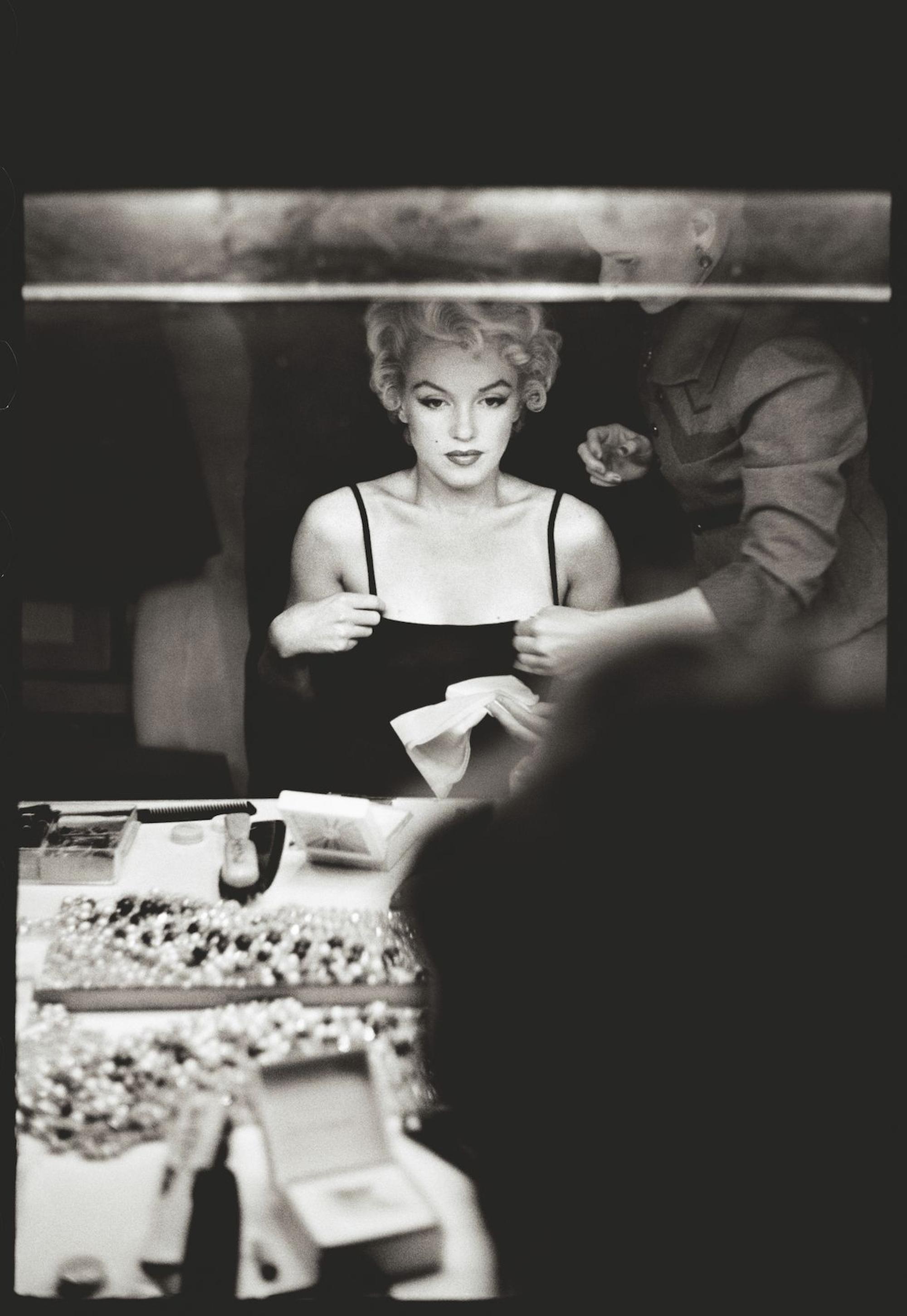 Marilyn Monroe sitzt am Schminktisch und blickt in einen Spiegel.