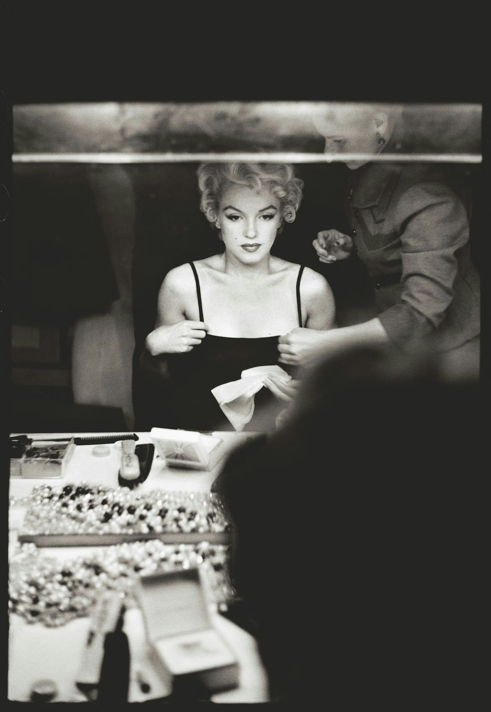 Marilyn Monroe sitzt am Schminktisch und blickt in einen Spiegel.