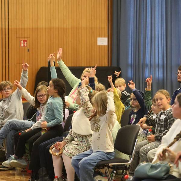 Ein Mann mit Mikrofon vor Schülerinnen und Schülern, die sich melden.