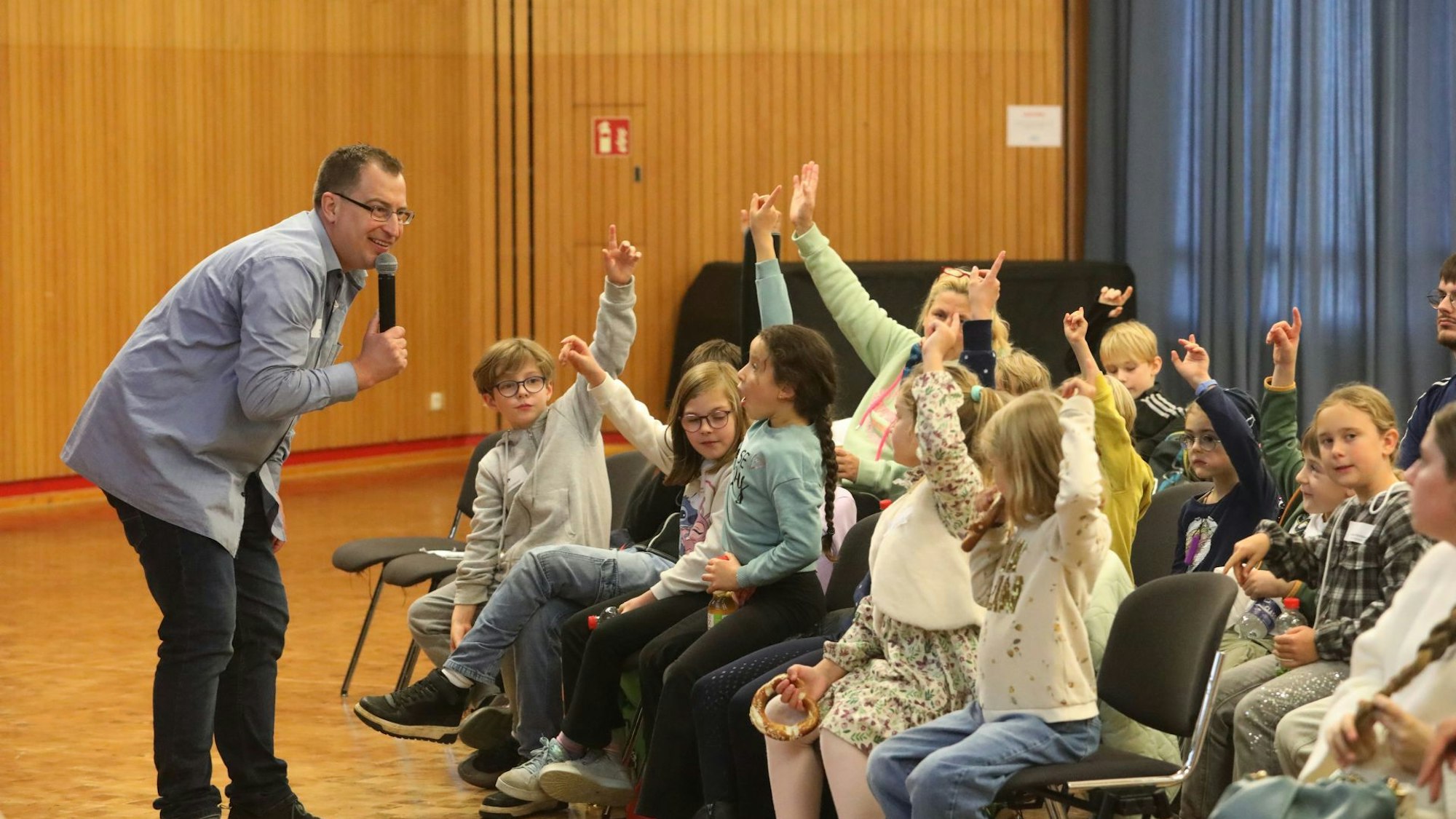 Ein Mann mit Mikrofon vor Schülerinnen und Schülern, die sich melden.