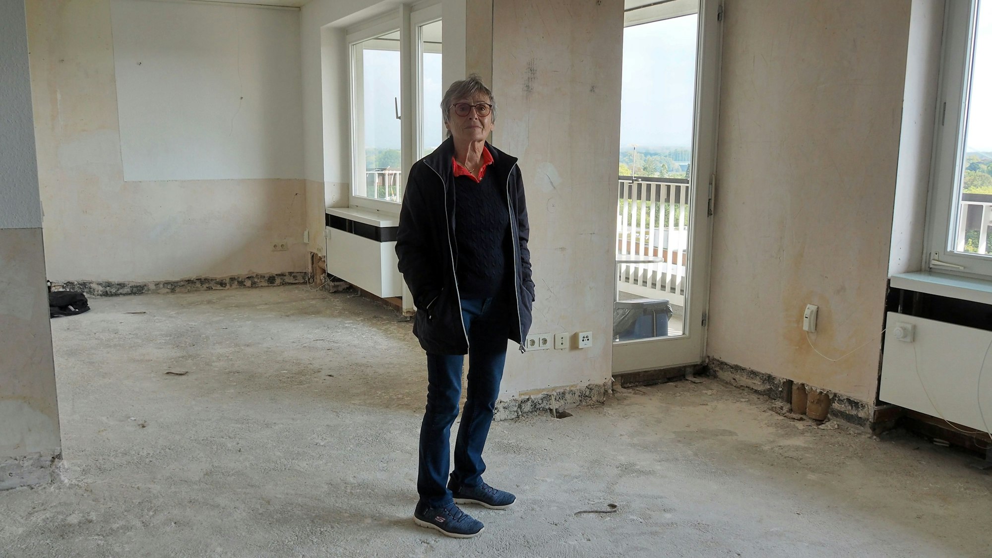 Eine ältere Frau steht in einer leeren, sanierungsbedürftigen Wohnung.
