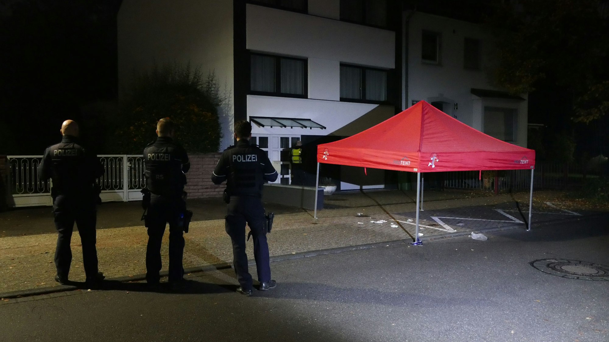 Drei Polizeibeamte stehen auf der Straße vor einem roten Pavillon.