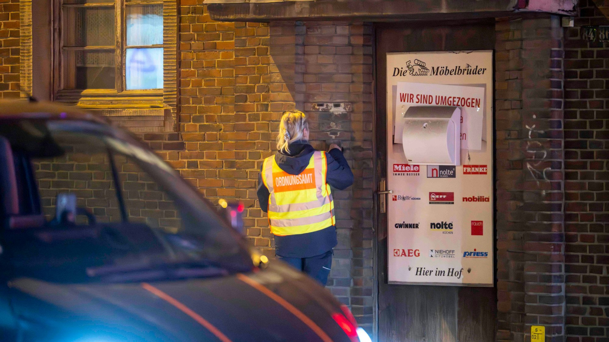 Eine Frau trägt eine Warnweste mit dem Schriftzug Ordnungsamt und klingelt an einer Haustür, um Menschen über eine Evakuierung in Euskirchen zu informieren.