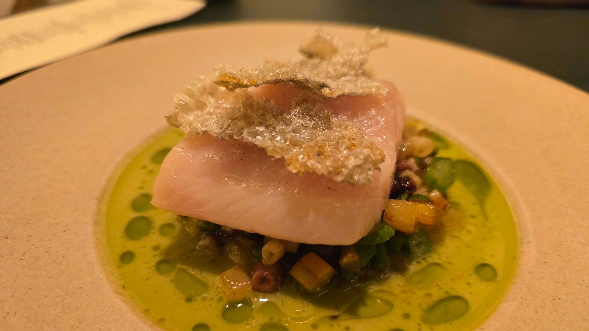 Ein Tellergericht ist zu sehen mit Fisch und grünem Saucenspiegel