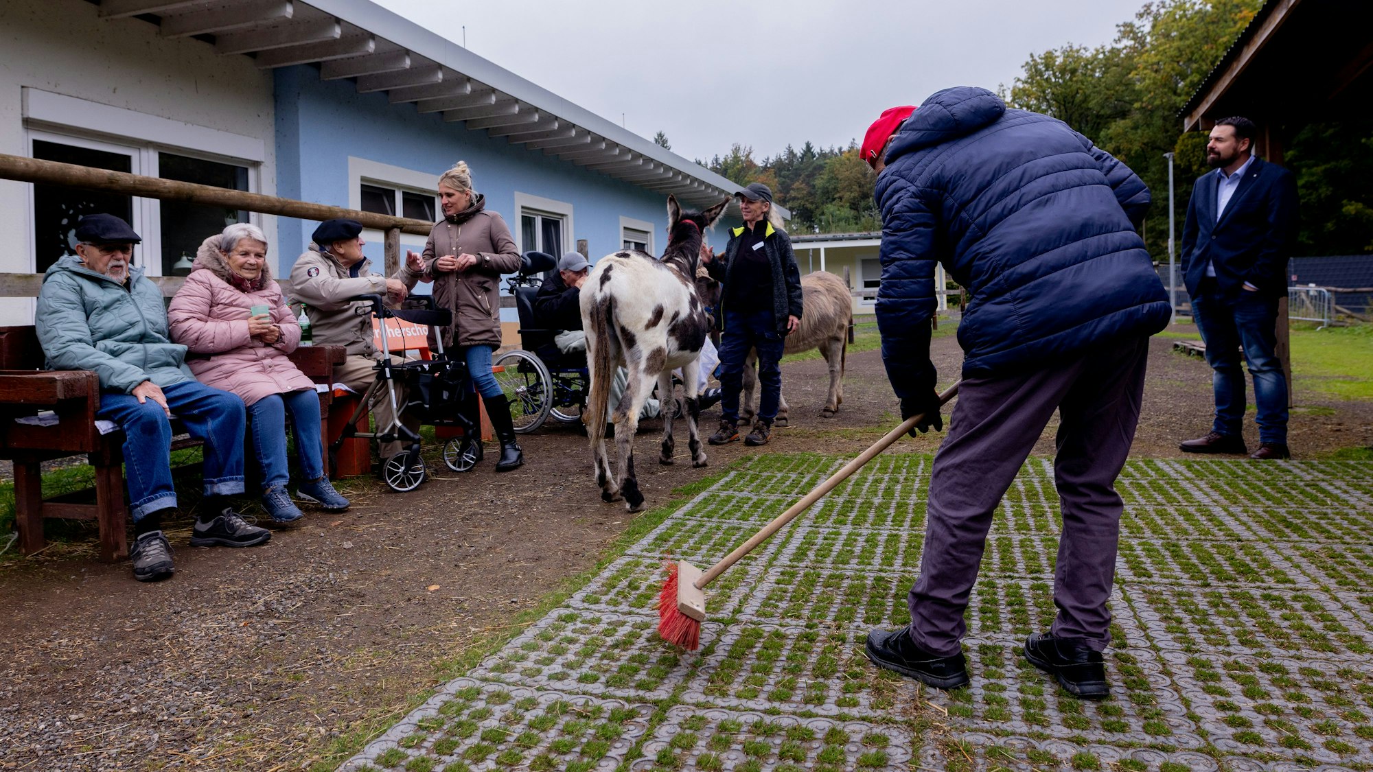 Matthias Offergeld fegt draußen einen Bereich, in dessen Nähe sich Menschen und Esel aufhalten.