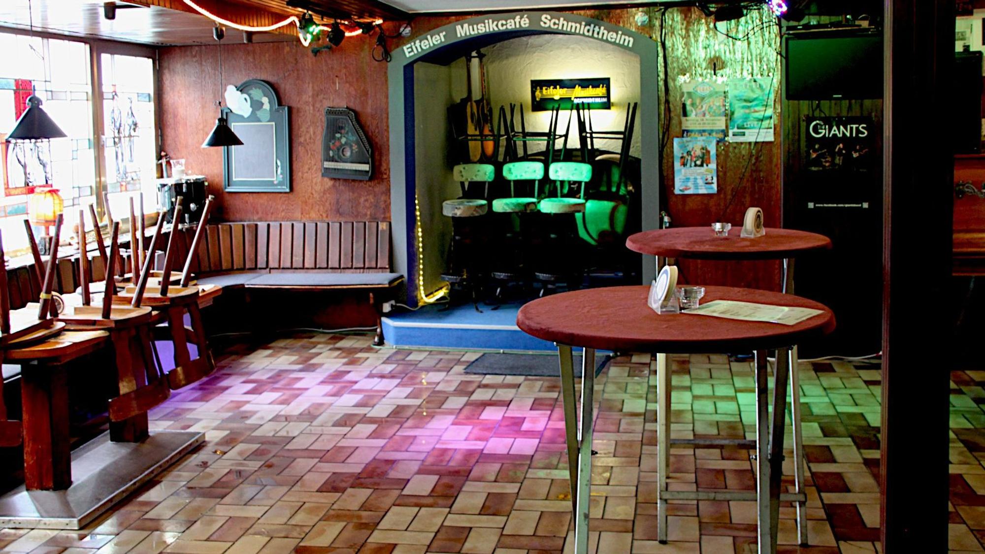 Blick in das „Eifeler Musikcafé“: Der Boden in der ehemaligen Gaststätte ist gefliest. Buntes Licht aus Scheinwerfern leuchtet darauf. Im Raum befinden sich zwei Stehtische.