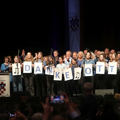 Zwei Chöre auf der Bühne, die in der ersten Reihe auf großen Blättern mit einzelenen Buchstaben „Danke Otto“ zeigen.