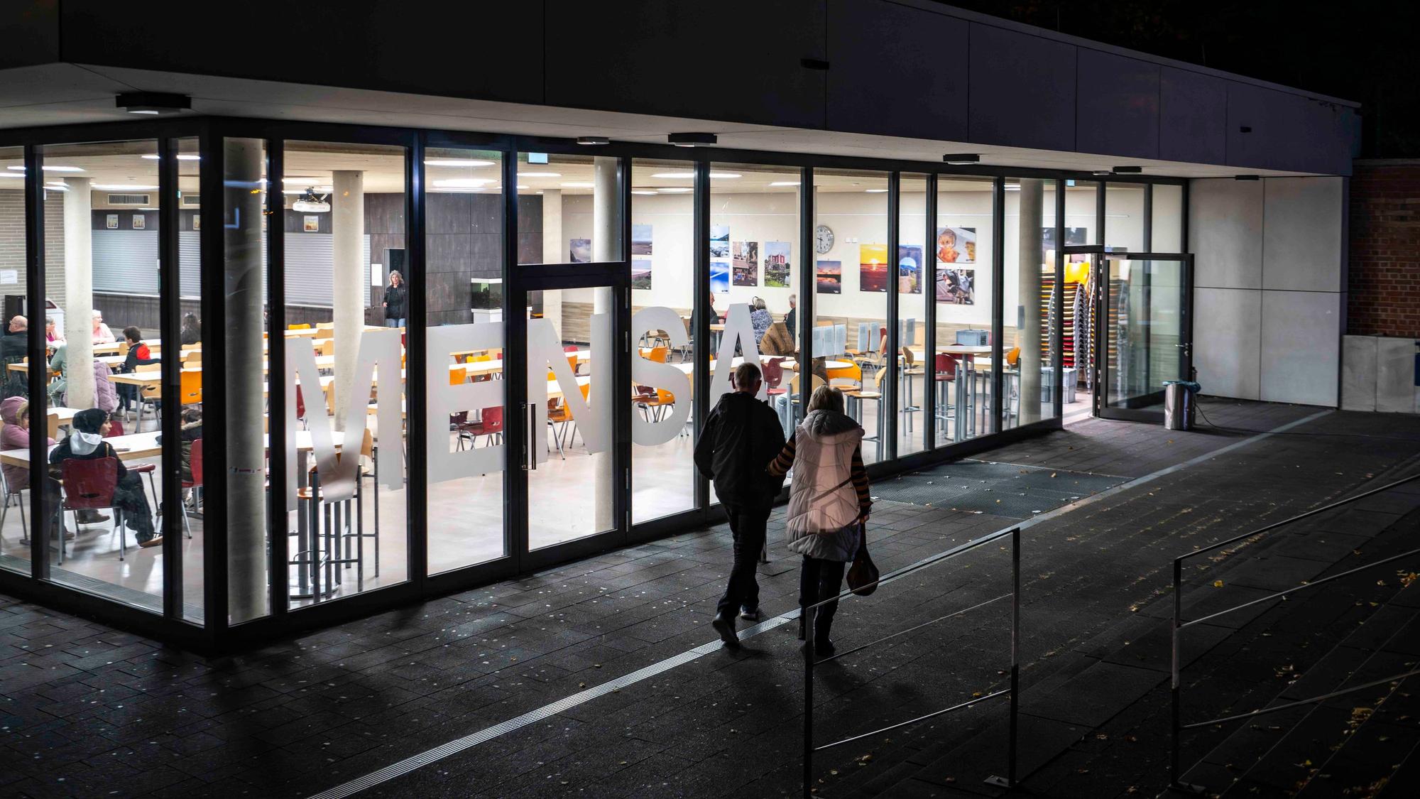 Das Bild zeigt die Mensa der Gesamtschule in Euskirchen. Zwei Menschen machen sich gerade auf den Weg zur Sammelstelle für die Evakuierten.