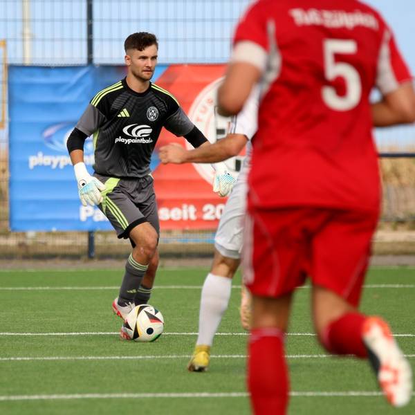 Torwart Jan Beyers hat den Ball am Fuß und schaut nach vorne, um sich einen Überblick zu verschaffen. Im Vordergrund ist unscharf ein Verteidiger von hinten zu sehen.
