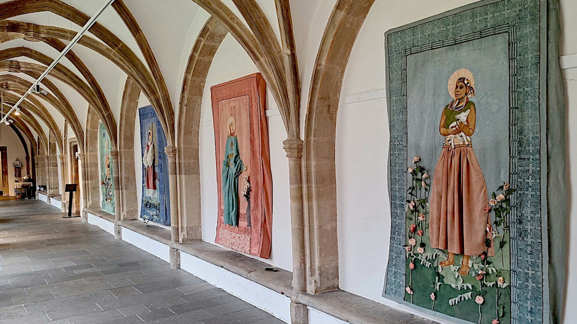 Sicht auf den gotischen Kreuzgang des Klosters Steinfeld. In den Wandnischen hängen Textilien, die mit Blumen verziert wurden.