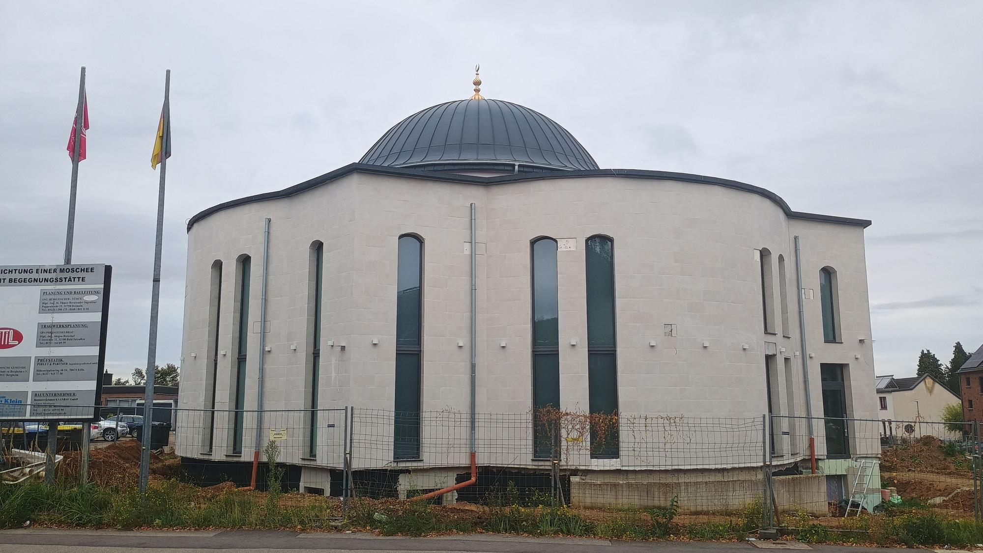 Zu sehen ist das Gebäude der Moschee. Die gebogenen Fenster sind sehr lang und ziehen sich fast über die gesamte Höhe des Gebäudes. Oben ist eine Kuppel.