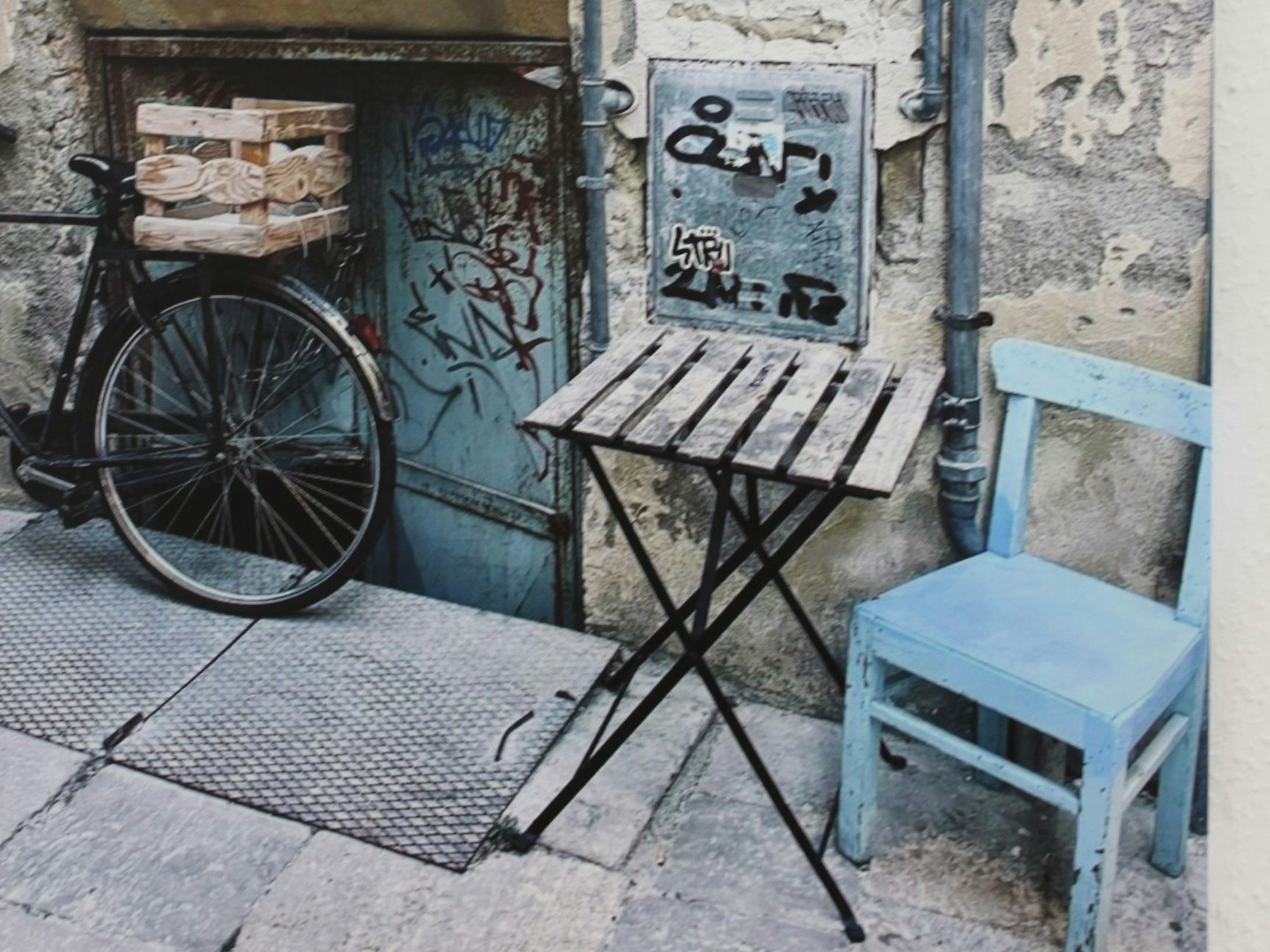 Ein blauer Stuhl steht neben einem Tisch und einem Fahrrad draußen an einer Straße.