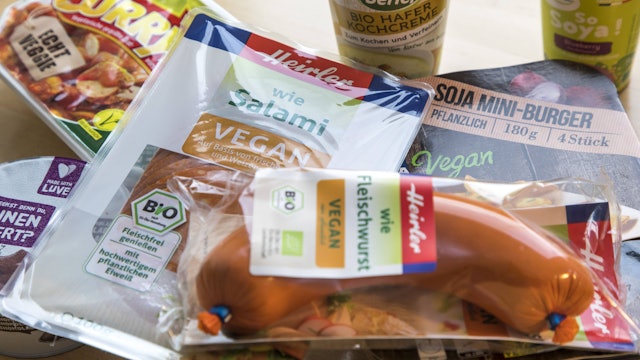 Vegane und vegetarische Fertigprodukte, wie fleischlose Salami und Fleischwurst, Currywurst, Burger und Joghurt, liegen oder stehen auf einem Tisch.