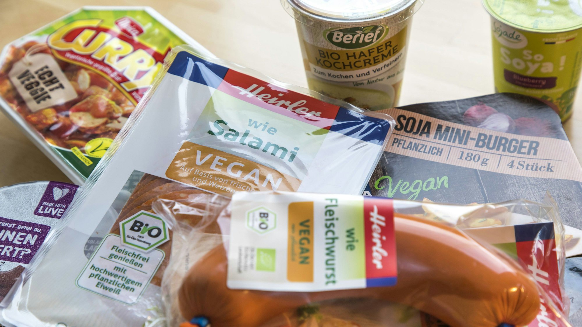 Vegane und vegetarische Fertigprodukte, wie fleischlose Salami und Fleischwurst, Currywurst, Burger und Joghurt, liegen oder stehen auf einem Tisch.