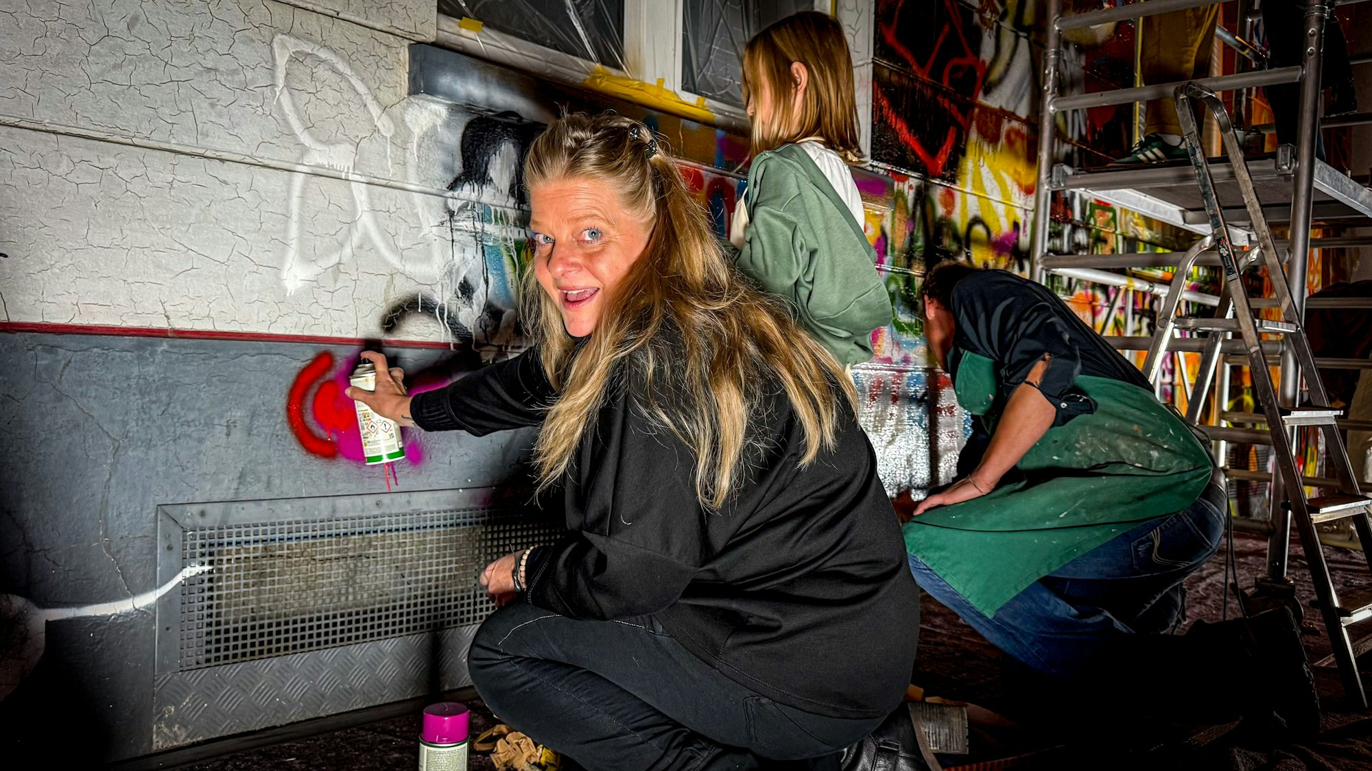 Drei Frauen sprühen bunte Farbe auf eine Wand.
