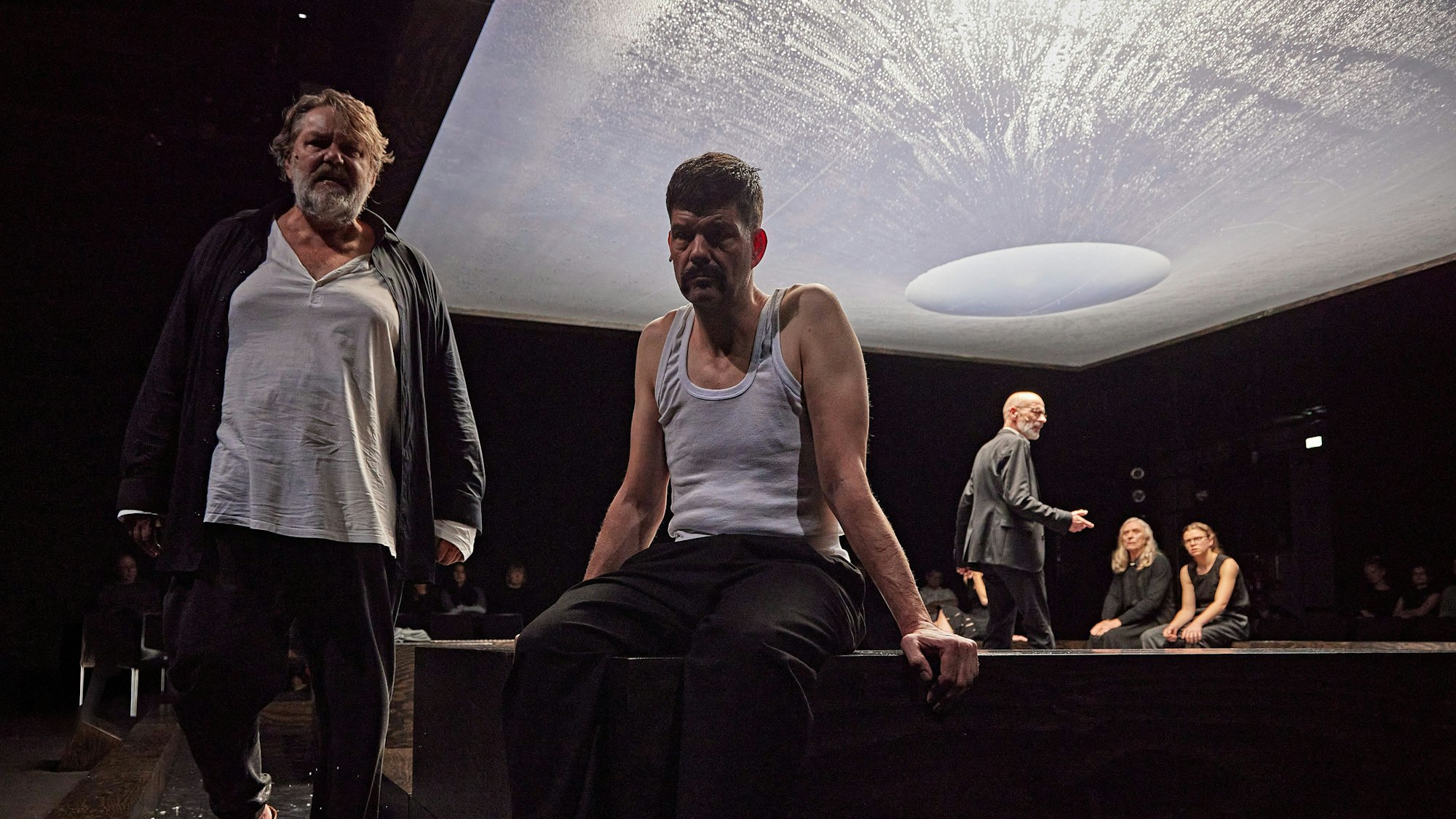 Andreas Becks steht links im Bild, Frank Genser sitzt daneben. Im Hintergrund sieht man den Rest des Ensembles, darüber den mit Wasser gefüllten Baldachin.