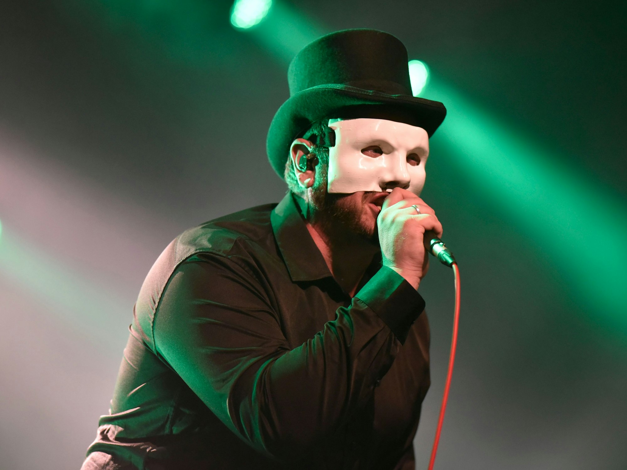 Das Bild zeigt einen Sänger, der eine Maske und einen Zylinderhut trägt.