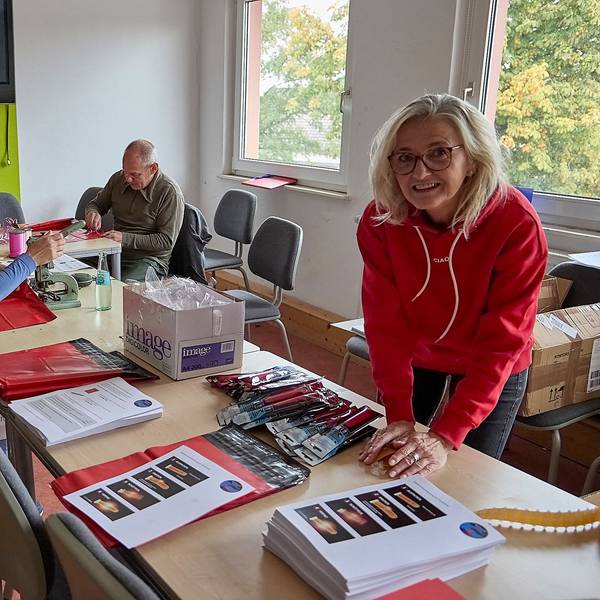 Simone Uhlig, Ines Hermanns, Burkhard Rosenbaum und Andrea Breuer (von links) befüllen rote Tüten. Auf einem Tisch liegen ausgedruckte Anleitungen und Knicklichter.