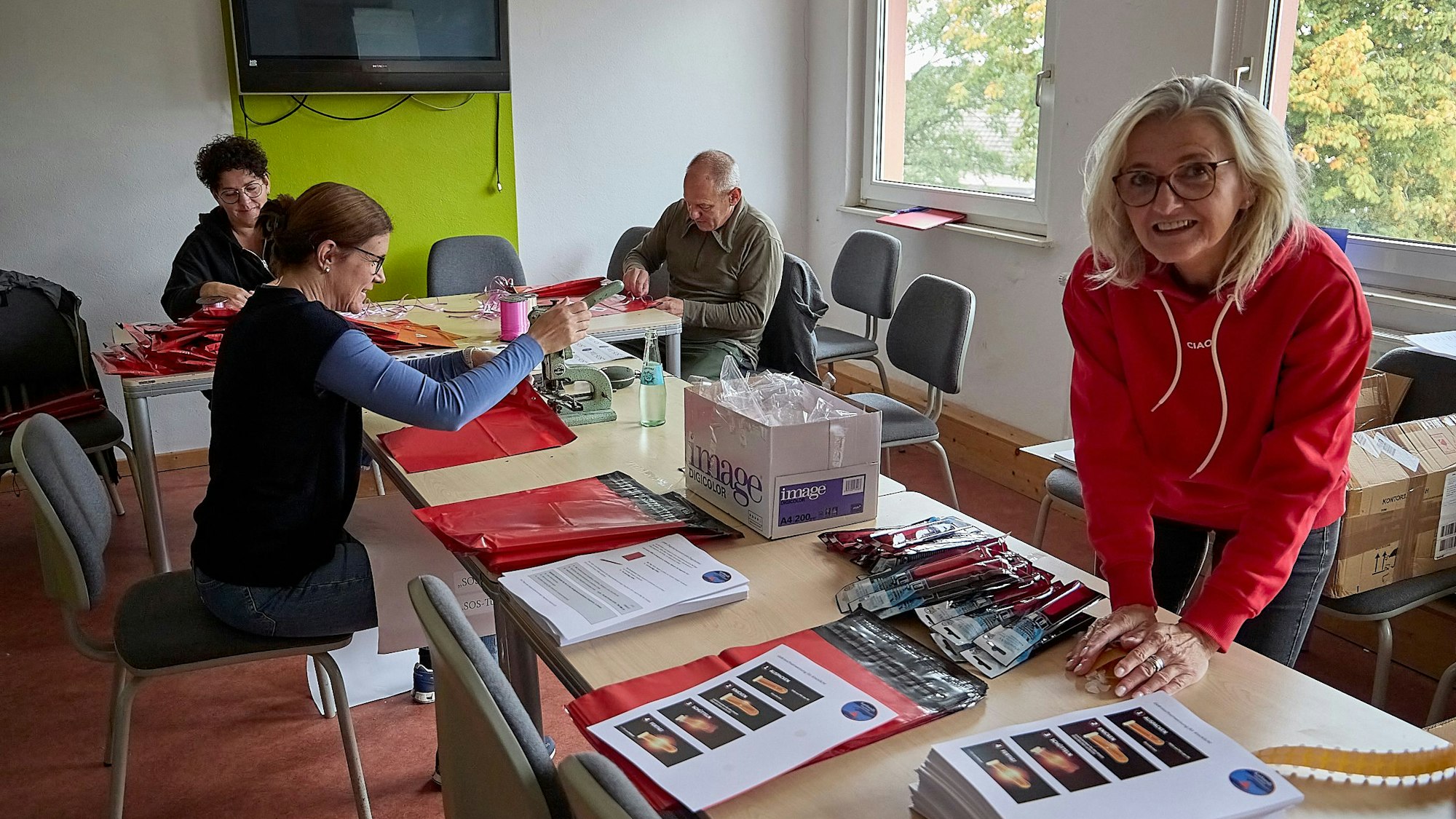 Simone Uhlig, Ines Hermanns, Burkhard Rosenbaum und Andrea Breuer (von links) befüllen rote Tüten. Auf einem Tisch liegen ausgedruckte Anleitungen und Knicklichter.