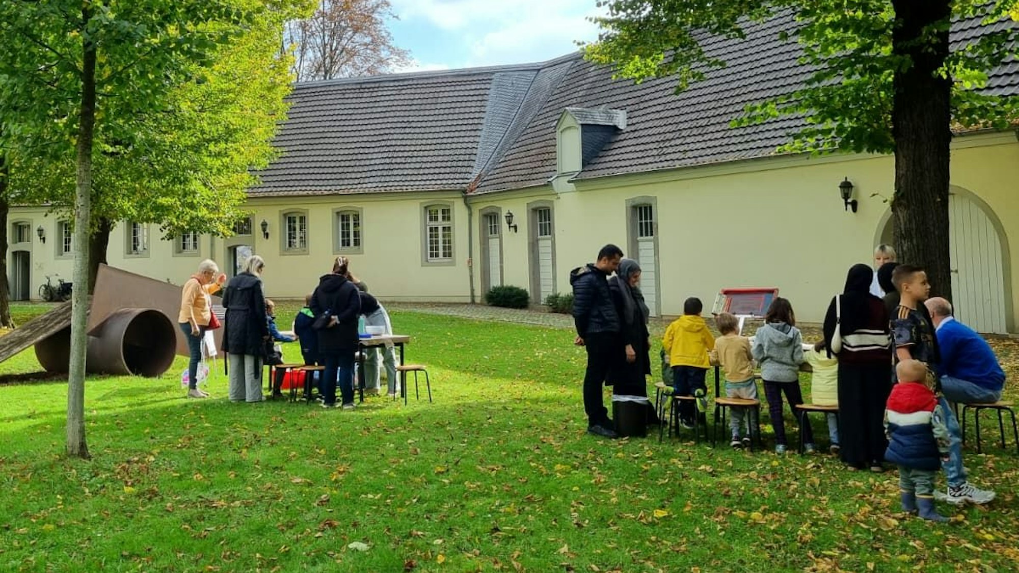 Menschen stehen an Tischen und Bänken im Innenhof von Schloss Morsbroich.