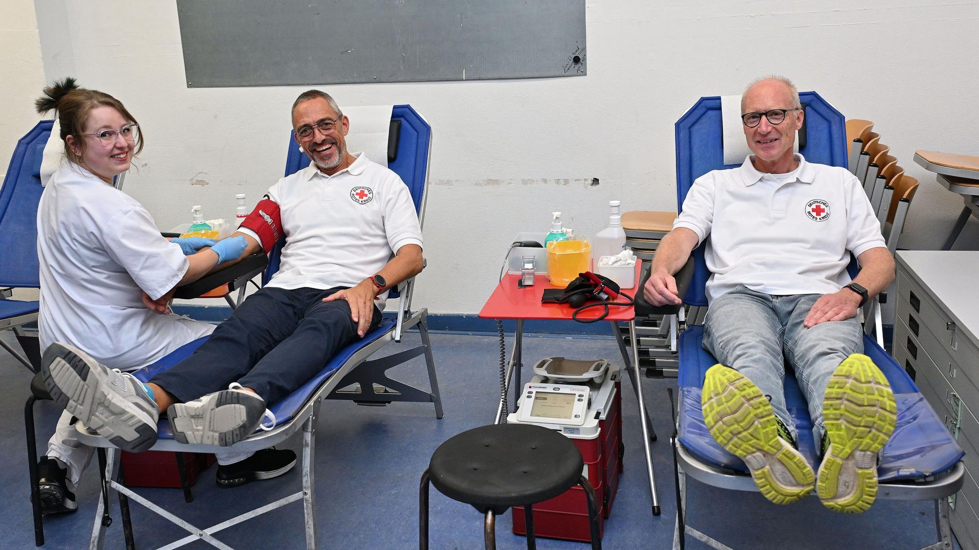 Zwei Männer sitzen auf Liegen und bekommen von einer Krankenschwester Blut abgenommen.