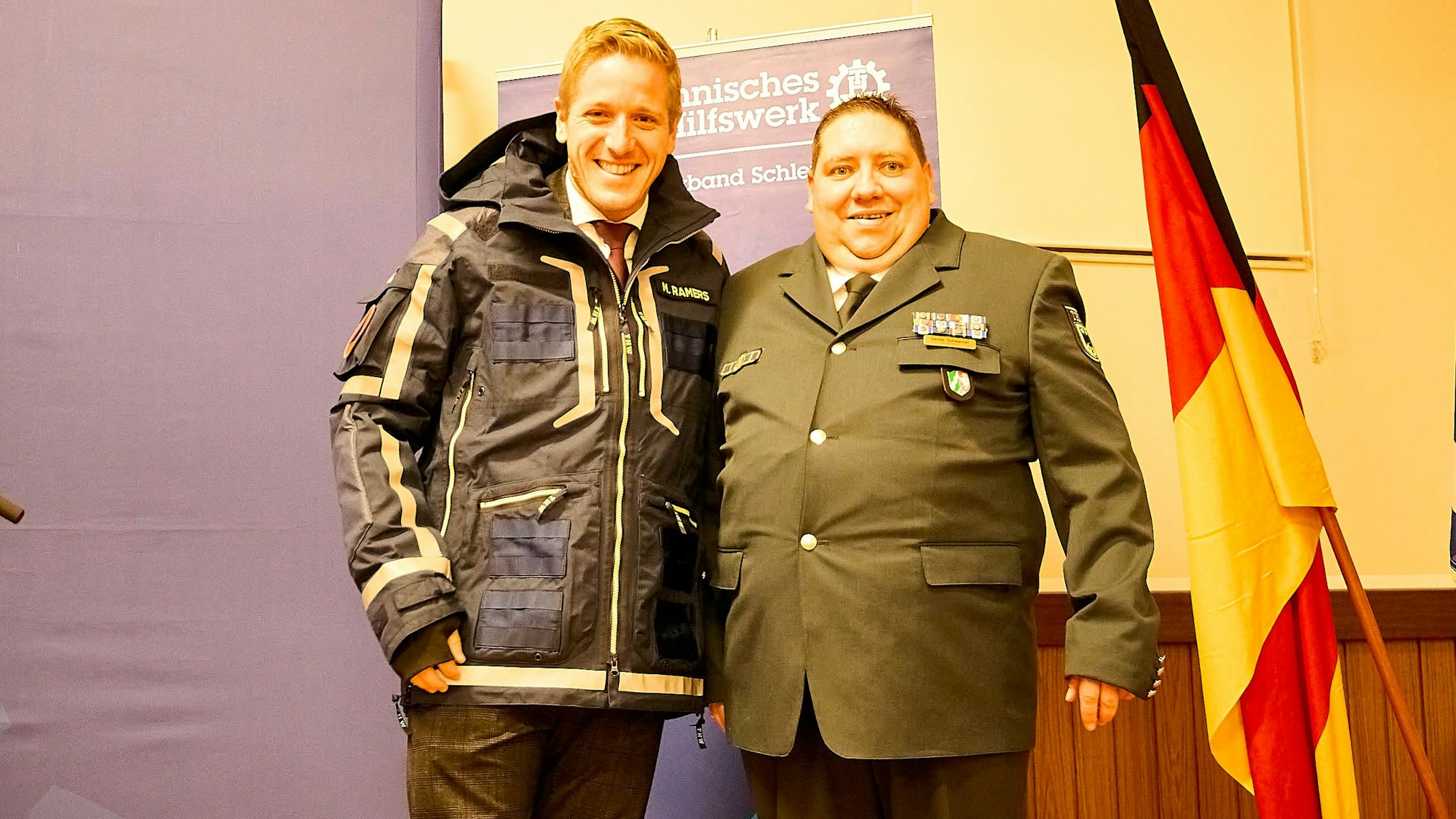 Markus Ramers steht in THW-Einsatzkleidung neben Daniel Schwarzer – beide grinsen.