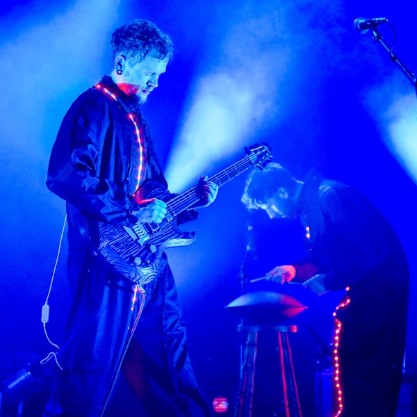 Das Bild zeigt einen Gitarristen und einen weiteren Musiker auf einer Bühne.