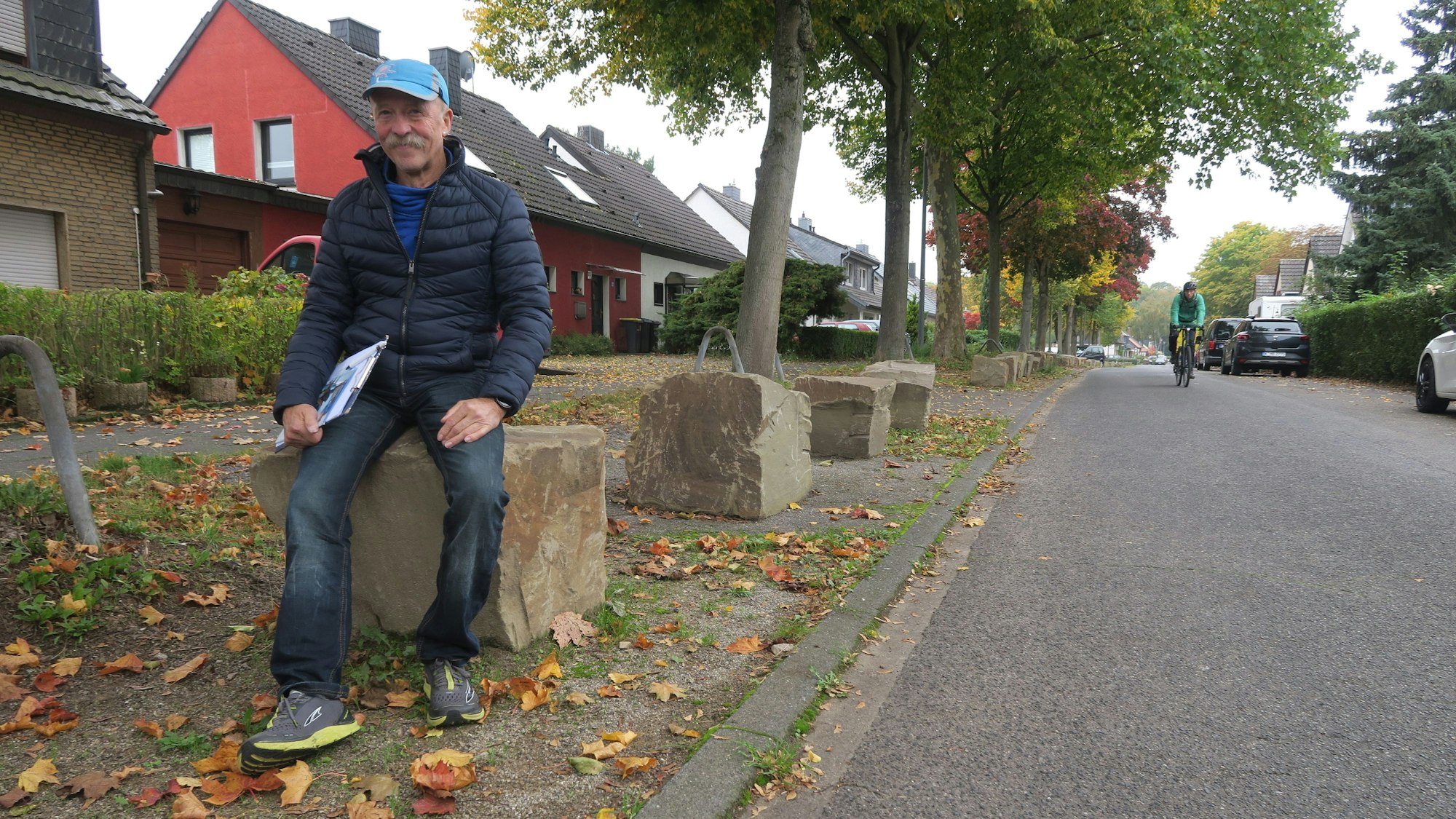 Ein Mann mit blauer Kappe und Klemmbrett unter dem Arm sitzt auf einem massiven Felsbrocken.