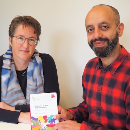 Eine Frau und ein Mann mit Bart sitzen nebeneinander an einem Tisch.