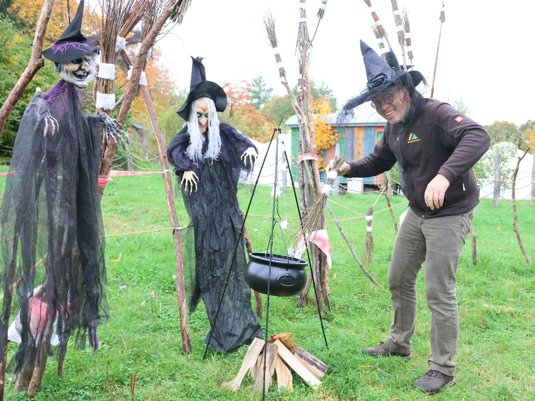 Ein Mann steht inmitten von Hexenfiguren auf einer Wiese.