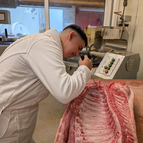 Ein junger Mann schneidet mit einem Messer an einer Schweinehälfte.