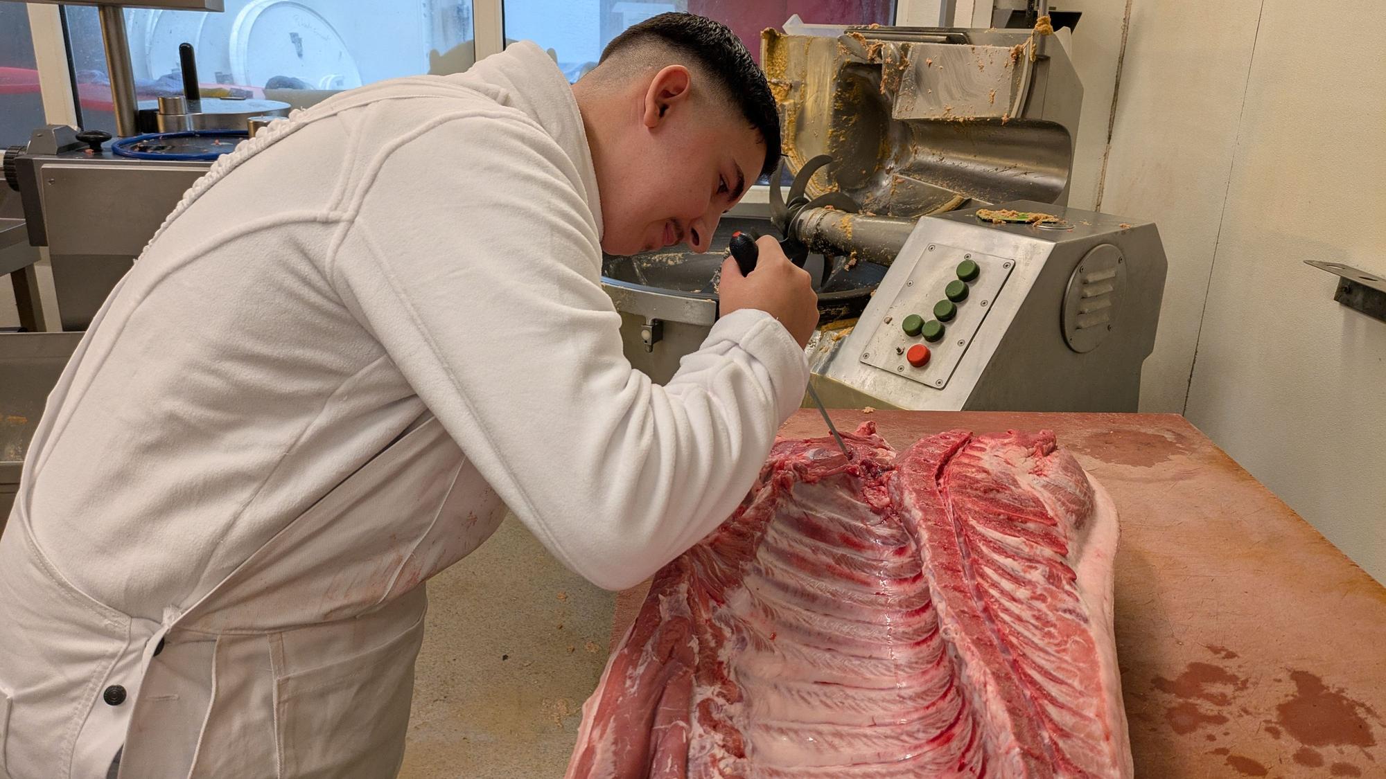 Ein junger Mann schneidet mit einem Messer an einer Schweinehälfte.