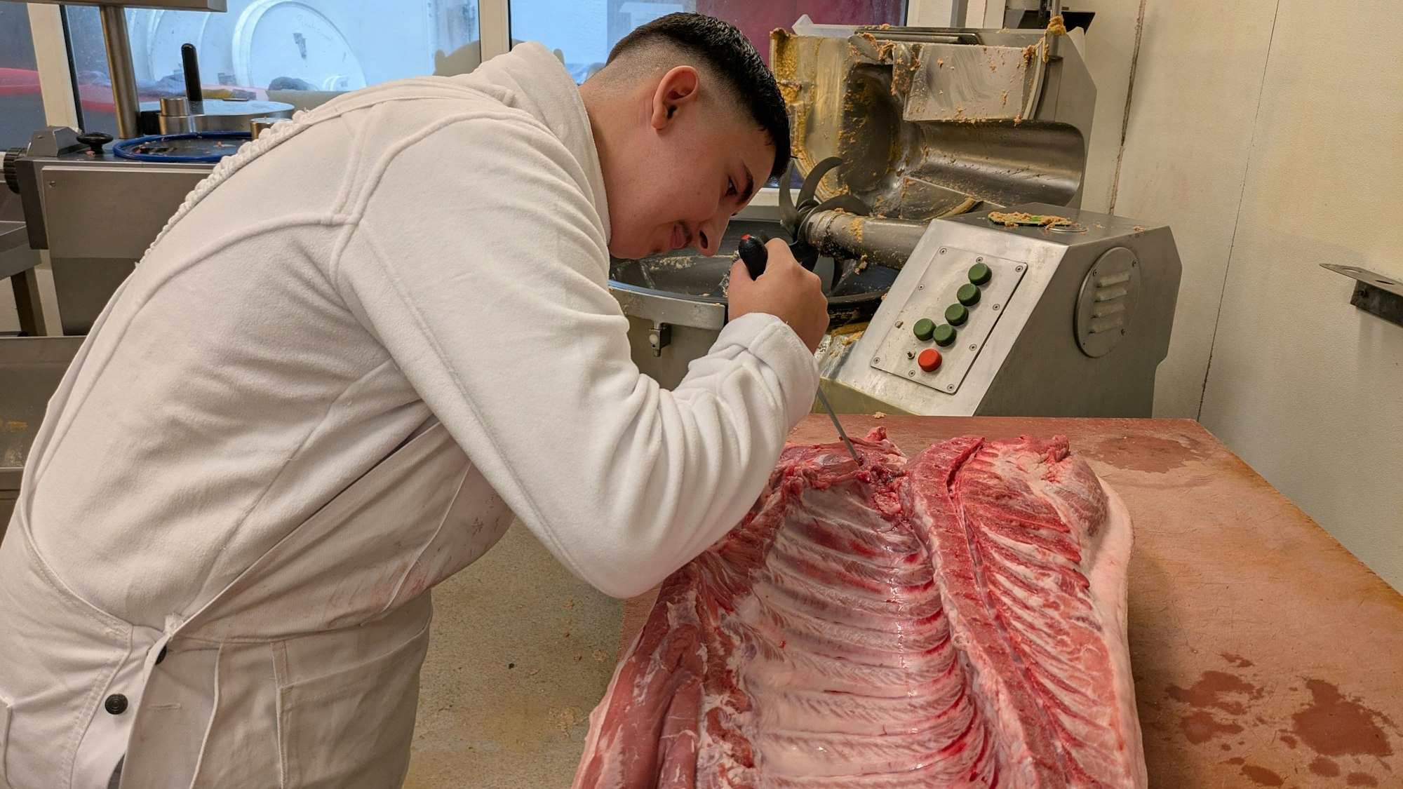 Ein junger Mann schneidet mit einem Messer an einer Schweinehälfte.