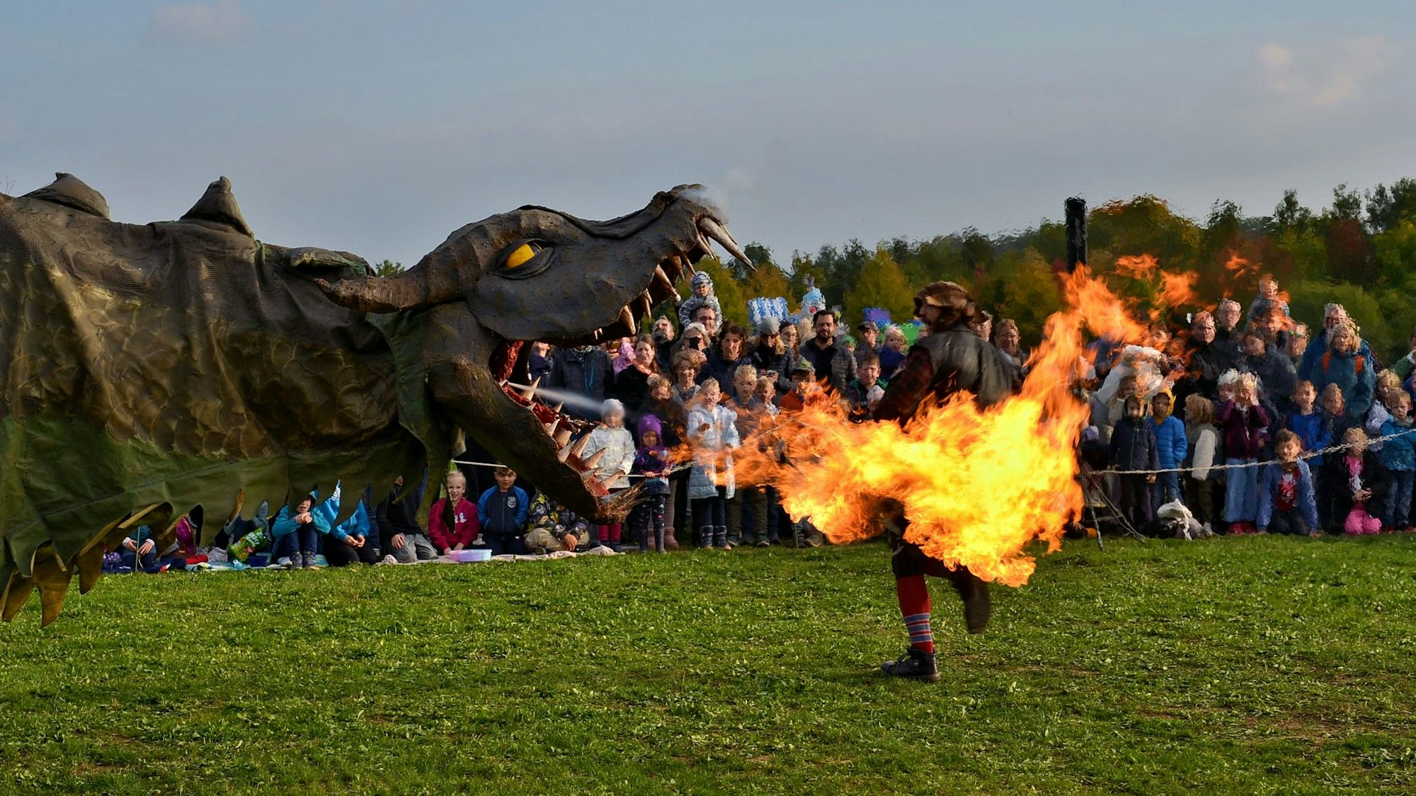 Aus einer Drachen-Konstruktion kommt Feuer. Vor den Flammen läuft ein verkleideter Räuber davon. Im Hintergrund schaut eine Menge der Inszenierung zu.