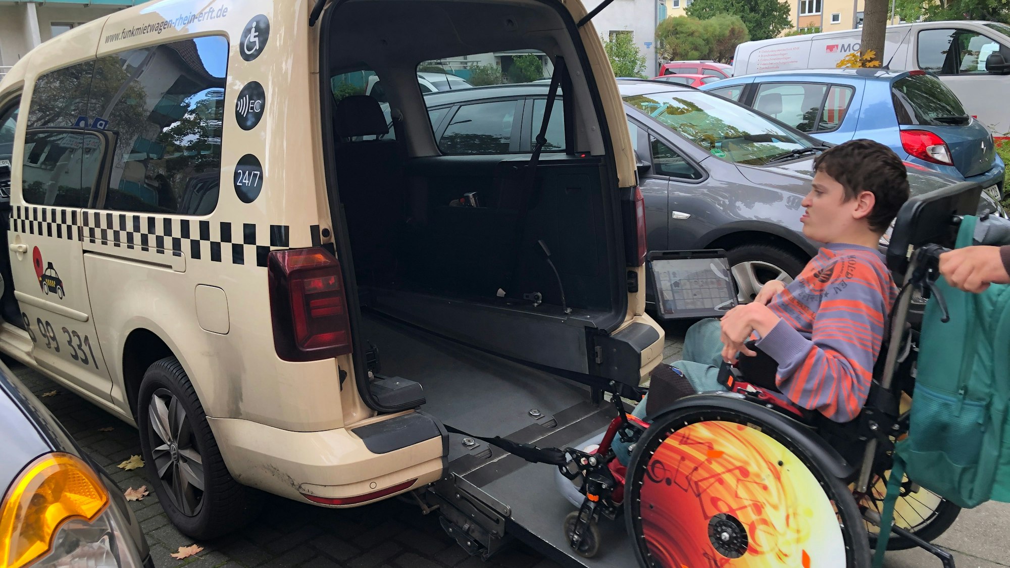 Ein junger Mann im Rollstuhl wird in ein Behinderten-Taxi verladen.