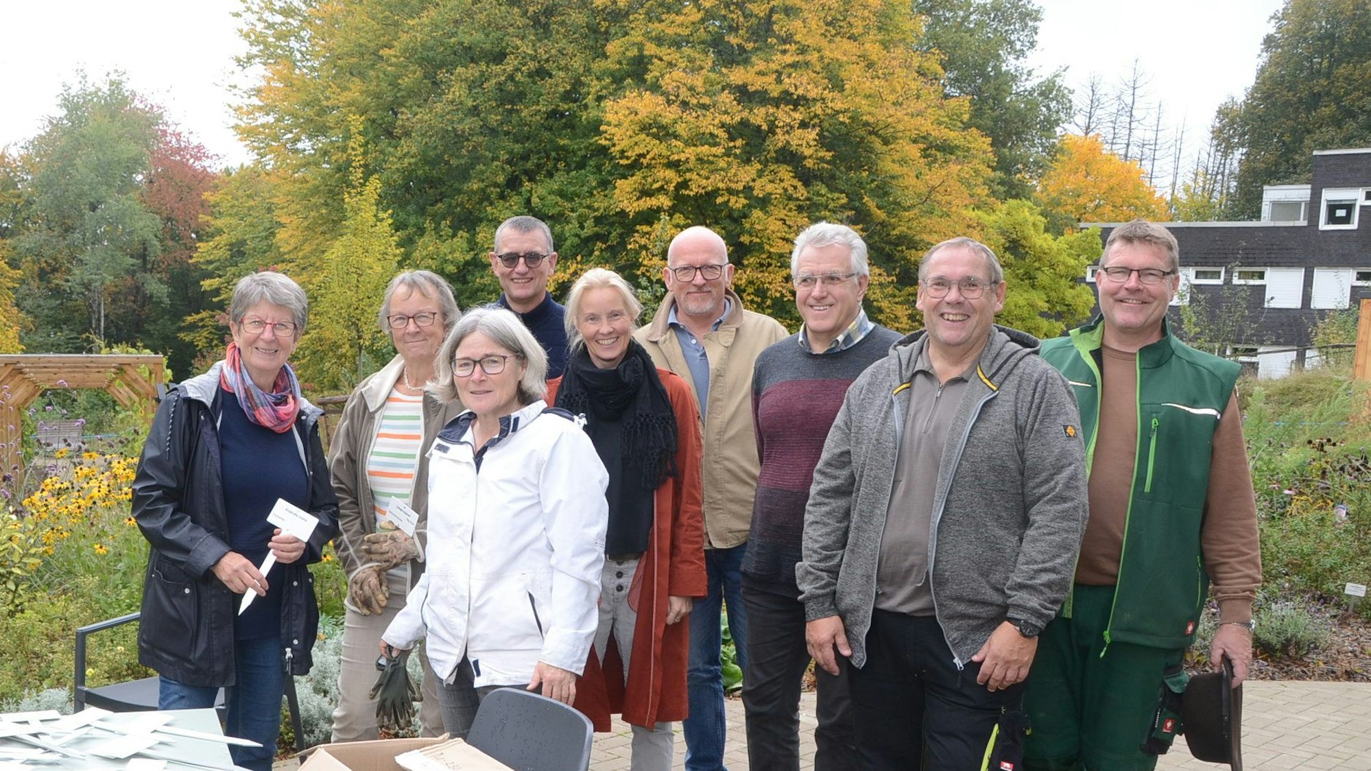 Männer und Frauen stehen in einem herbstlichen Garten.