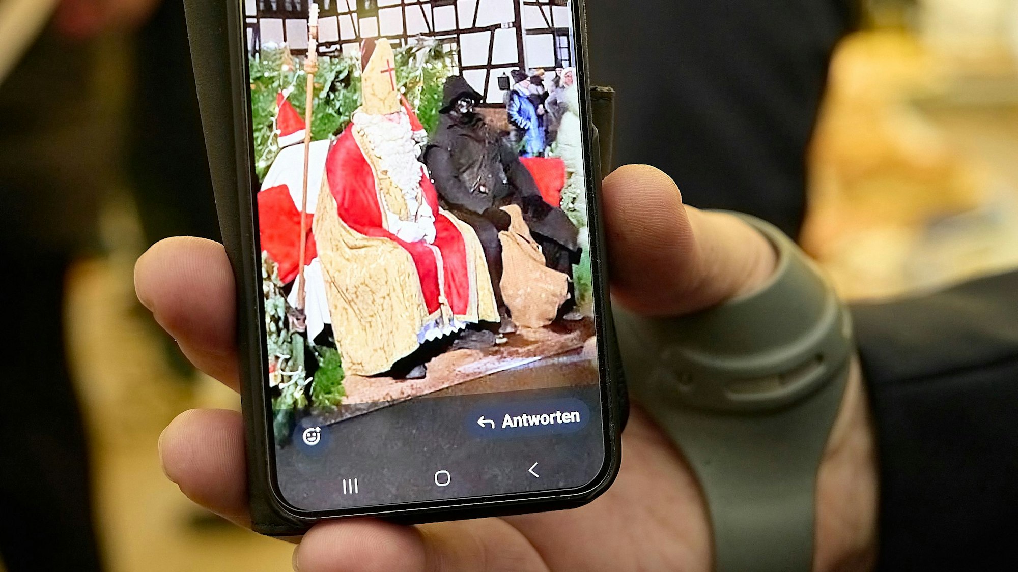 In einer Hand ruht ein Handy, auf dem ein Foto von zwei Menschen geöffnet ist, die als Nikolaus und Hans Muff verkleidet sind.