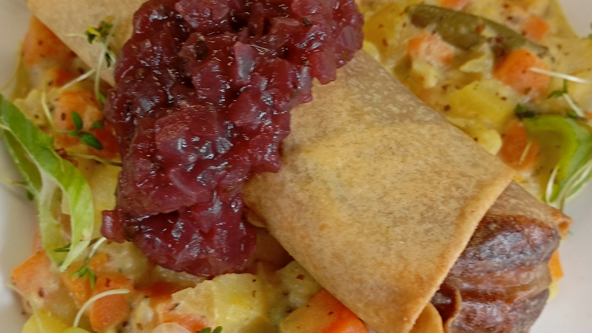 Das Bild zeigt eine Frühlingsrolle, die auf Gemüse auf einem Teller angerichtet ist.