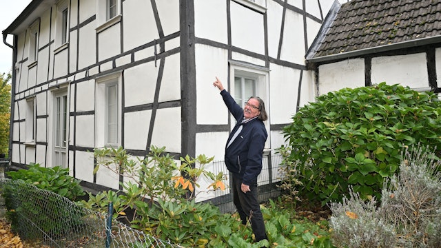 Ein Mann deutet auf die Außenbalken eines bergischen Fachwerkhauses.